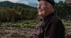 Portrait d’un homme âgé assis dans son jardin, souriant, sous un ciel bleu et lumineux