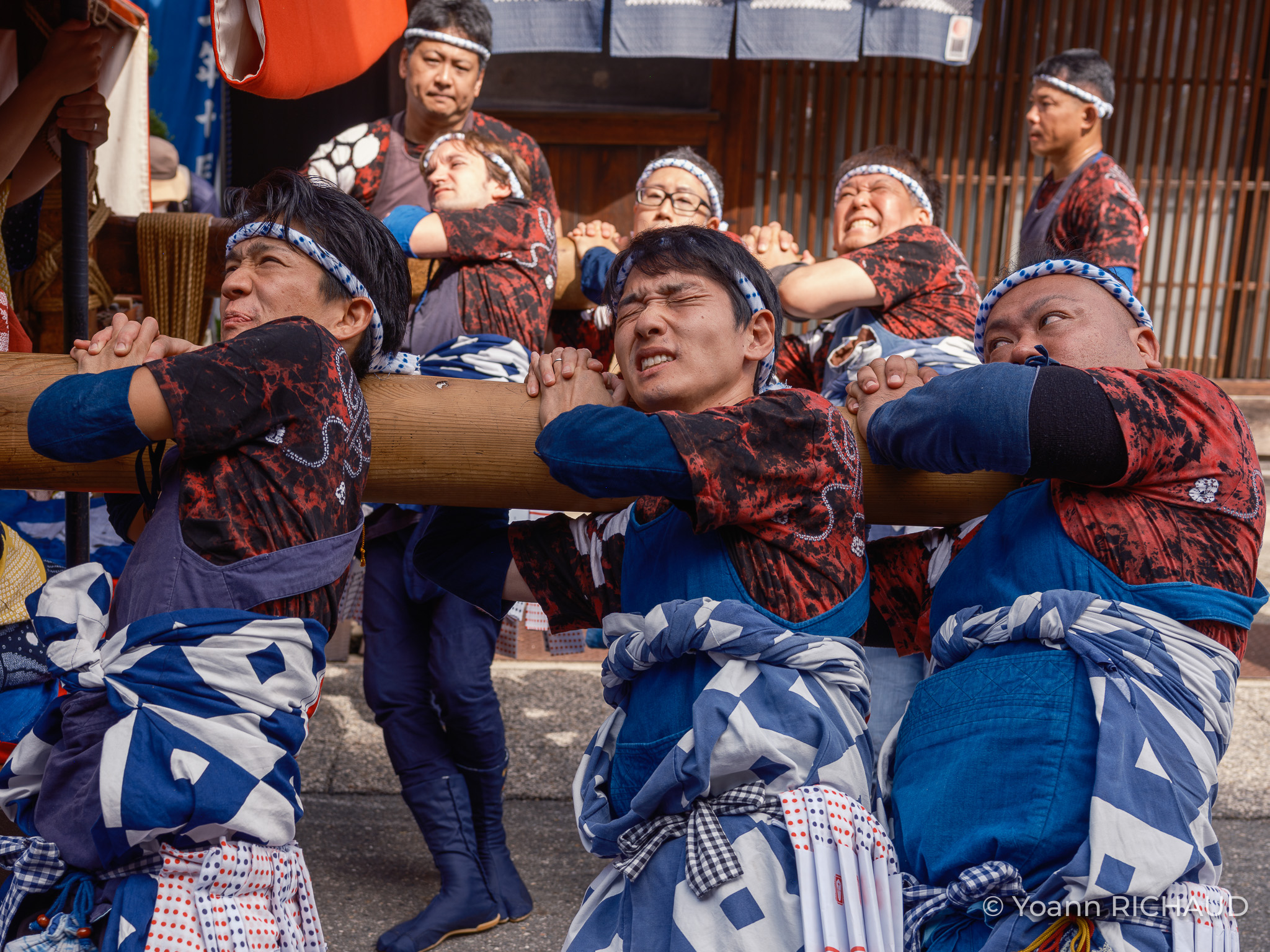 Groupe de personnes en tenue bleue et rouge portant ensemble une structure pendant une fête.
