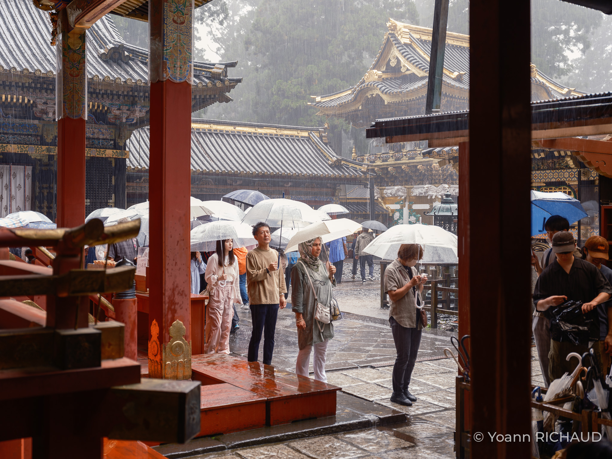 Visiteur·rices portant des parapluies transparents dans l’enceinte d’un temple sous la pluie.