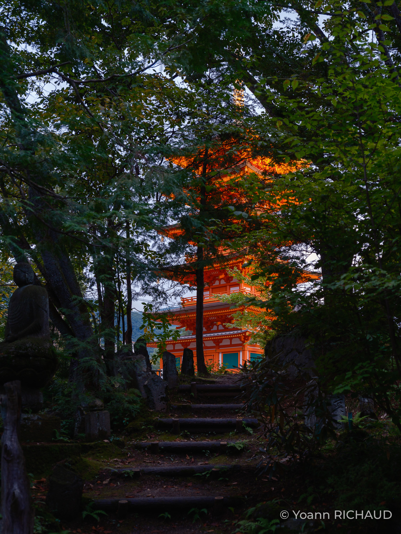 Escalier de pierre montant vers une pagode rouge entre les arbres.