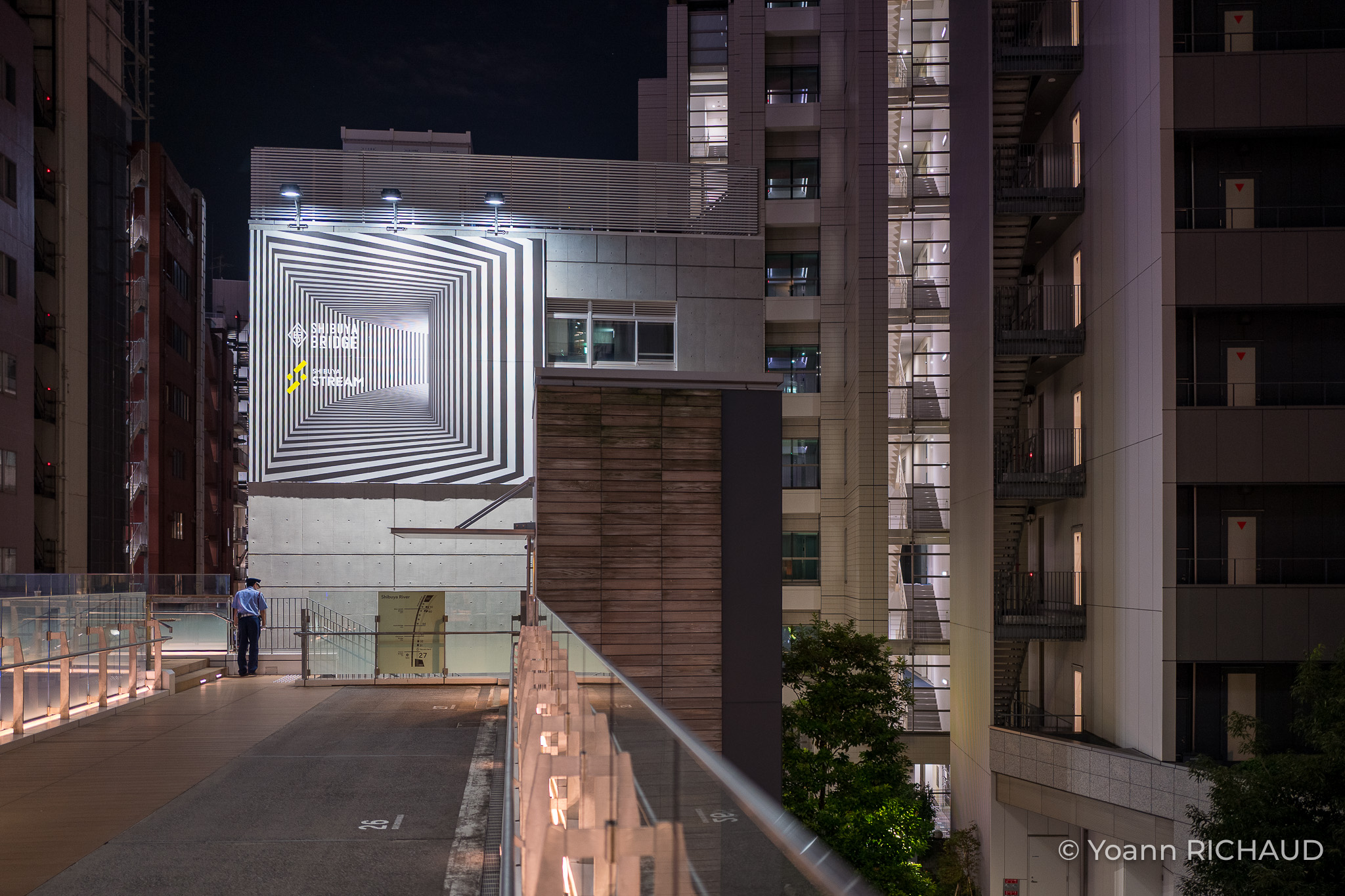 Passage urbain de nuit face à une projection lumineuse géométrique.